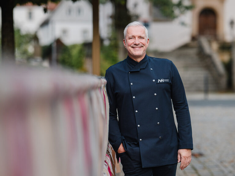 Der Koch Alexander Herrmann steht vor einem Zaun.