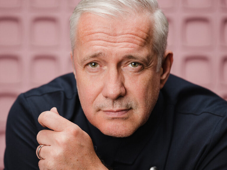 Ein Mann mit weißem Haar und einer analogen Uhr am Handgelenk.