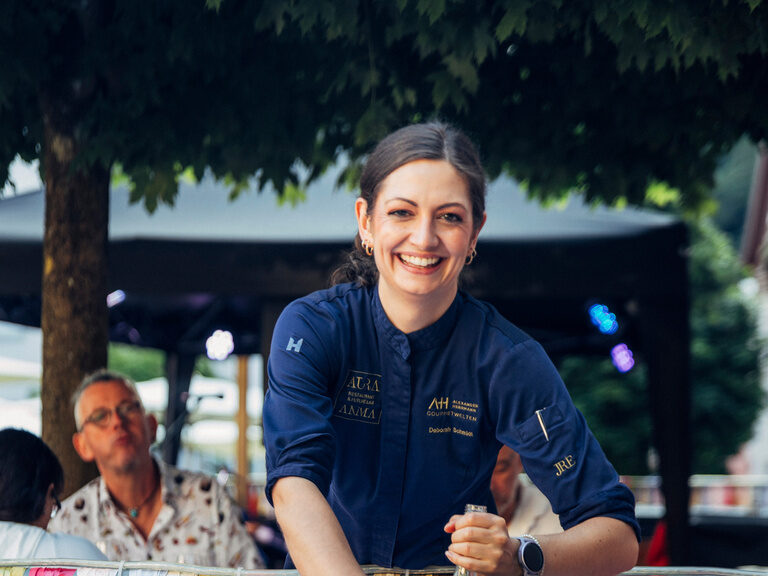 Eine Frau in blauer Kleidung bereitet Essen in einer Küche zu.
